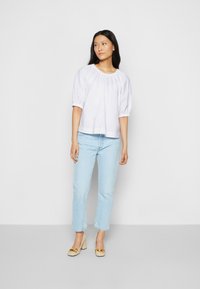Blusa de algodão branca com mangas curtas bufantes e decote franzido, combinada com jeans de perna reta azul claro e sapatos de salto bloco bege.