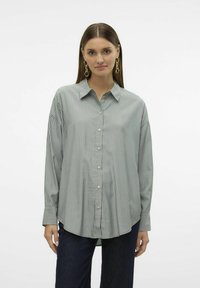 Camicia a righe in verde chiaro e bianco, con collo, maniche lunghe e orlo curvato. Il tessuto appare liscio e leggero.