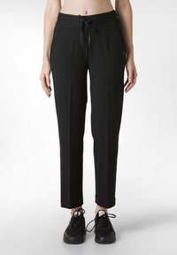 Schwarze, taillierte Jogginghosen mit elastischem Bund und Kordelzug, ausgestattet mit Seitentaschen und einer glatten Textur. Getragen mit schwarzen Sportschuhen.