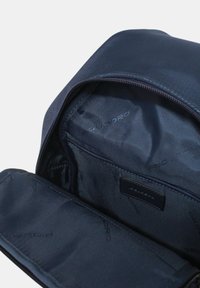 Zaino blu scuro aperto per mostrare la fodera interna con diverse tasche e il logo del marchio stampato sul tessuto e sull'etichetta.