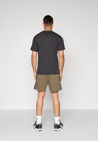 Melna īsroku T-krekls ar apaļu apkakli, kombinēts ar olīvzaļām sporta šortiem, baltām zeķēm un melniem sporta apaviem.