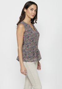 Blusa senza maniche con stampa floreale, scollatura a V e orlo peplum. Presenta un motivo colorato su un tessuto leggero. Abbinata a pantaloni beige.