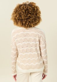 Gebreide cardigan in beige met een wit zigzagpatroon. Lange mouwen en geribde zoom. Geweven stof met een open structuur.