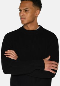 Pulover negru din tricot cu o textură textilă, gât rotund și mâneci lungi. Materialul este moale, cu detalii minime și croială confortabilă.