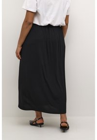 Zwarte, enkellange rok met elastische tailleband, gemaakt van een gladde stof. Gepaard met een eenvoudig wit t-shirt en zwarte sandalen.