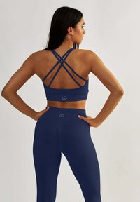 Granatowy zestaw odzieży sportowej składający się z sportowego biustonosza z ramiączkami na plecach oraz legginsów z wysokim stanem, o gładkiej fakturze i z logo na pasku w talii.
