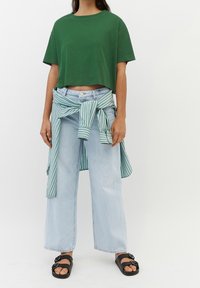 T-shirt verde cropped, jeans a gamba larga blu chiaro e una camicia a righe verdi e bianche legata in vita. Sandali neri completano il look.
