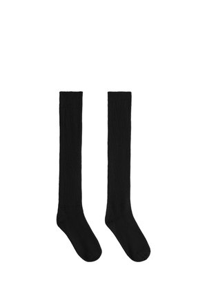 Paire de longues chaussettes noires côtelées posées à plat avec le pied pointant vers le bas sur un fond blanc.