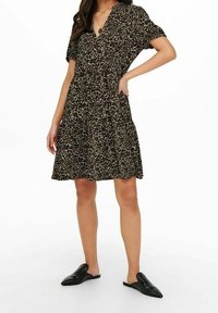 Robe noire avec un motif léopard, manches courtes, encolure en V et jupe fluide. Portée avec des chaussures noires à enfiler.