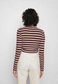 Langärmliges Oberteil mit maroon und beigen horizontalen Streifen, geripptem Textur und rundem Ausschnitt. Getragen mit hochgeschnittenen cremefarbenen Hosen.