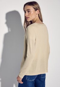 Stickad beige tröja med långa ärmar och rund halsringning. Slät textur med en något lös passform. Matchad med blå denimjeans.