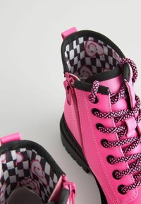 Stivaletti alla caviglia in ecopelle rosa con suola nera, interno a scacchi e lacci a motivo rosa e nero con chiusura a zip.