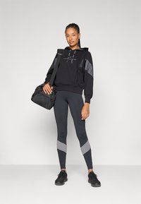 Svart hettegenser med grå detaljer, kombinert med tettsittende svarte leggings med grå chevronmønster. Svart treningsbag og joggesko.