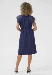 Navy dress with lace short sleeves, waist tie, and knee-length hem. Smooth fabric with a relaxed fit and delicate lace accents.