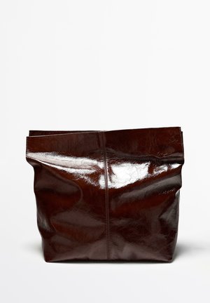Duża błyszcząca torebka typu tote z ciemnobrązowej skóry o miękkim, nieustrukturyzowanym kształcie na jednolitym białym tle.