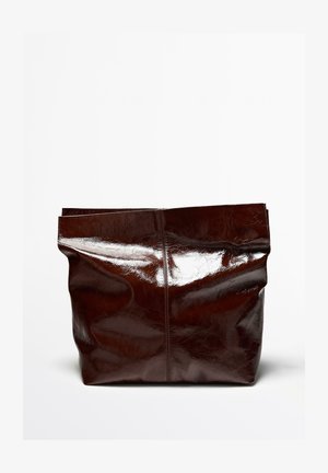 Stor blank mörkbrun läderväska med mjuk, ostrukturerad form mot en enfärgad vit bakgrund.