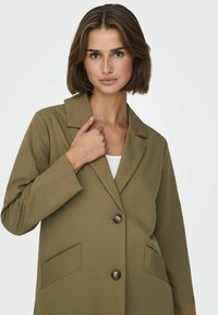 Blazer verde oliva realizzato in tessuto morbido, con colletto a risvolto, due tasche frontali e due bottoni neri per la chiusura.