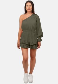 Rompers vert à une épaule avec un tissu texturé, une taille élastique et une jupe à volants superposés. Associé à des baskets blanches.