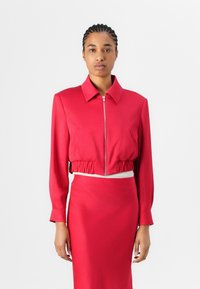 Red cropped jacket with a zip front, long sleeves, and elastic hem, paired with a matching fitted skirt. Smooth fabric, minimalist design.