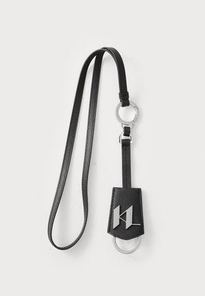 Porte-clés en cuir noir avec une finition texturée, comportant un anneau circulaire en argent et un accent de logo sur un support rectangulaire.