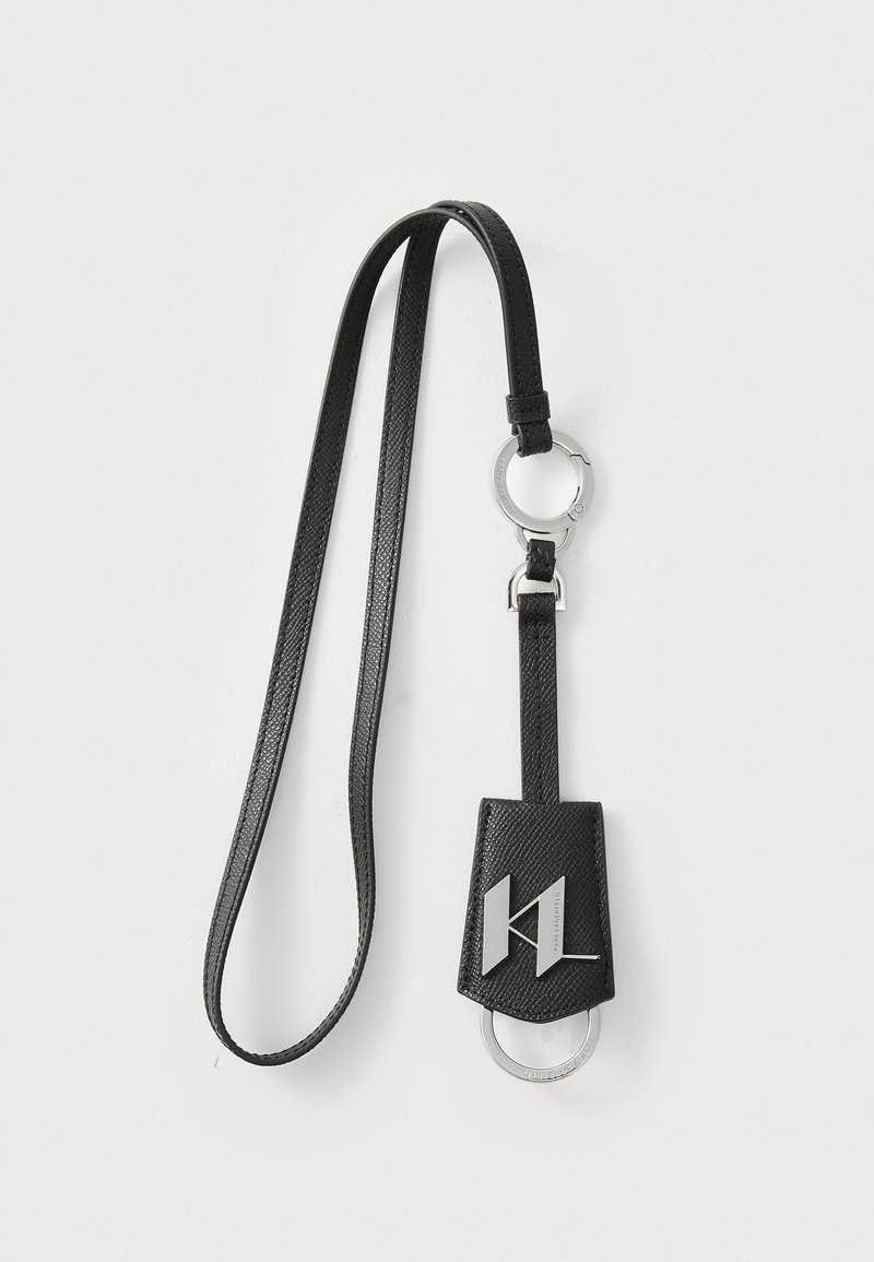 Porte-clés en cuir noir avec une finition texturée, comportant un anneau circulaire en argent et un accent de logo sur un support rectangulaire.