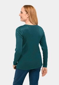 Türaubergine Langarmshirt mit geripptem Muster, runder Ausschnitt und leicht abgerundetem Saum. Getragen mit blauen Jeans, von hinten angesehen.
