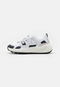 Weiße Sneaker mit schwarzen und grauen Akzenten, ausgestattet mit einem strukturierten Design, verstellbaren Riemen und einer dicken Gummisohle für Unterstützung.