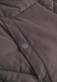 Dunkelbrauner, gesteppter Jackenstoff mit glatter Textur. Verfügt über einen schwarzen Knopfverschluss und diagonale Steppakzente.