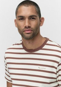 Randig t-shirt i krämvit och brun med en ribbad rund halsringning, som har ett strukturmaterial och en liten broderad logotyp på bröstet.