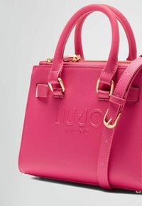 Sac à main texturé rose avec quincaillerie dorée, doté de poignées supérieures et d'une bandoulière amovible, détail de logo embossé sur le devant.