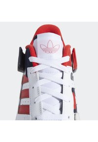 Baskets blanches Adidas avec des détails rouges et bleu marine, lacets blancs, doublure intérieure rouge, et le logo trefoil Adidas sur la languette.
