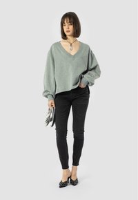 Szürke, oversized pulóver V-nyakkal, fekete skinny farmerral és pöttyös fekete magassarkúval párosítva. A modell egy ezüst színű clutch táskát tart.