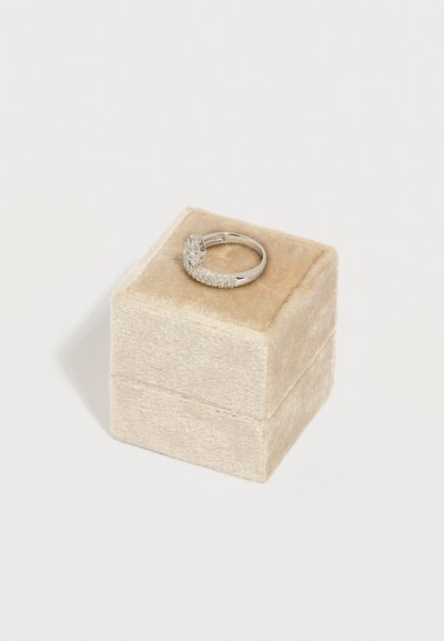 Ασημένιο δαχτυλίδι με στρογγυλό κεντρικό λίθο και μικρότερους λίθους στην μπάντα, τοποθετημένο πάνω σε μπεζ βελούδινο κουτί κοσμημάτων σε λευκό φόντο.