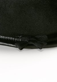 Nära bild av svart tyg med en liten dekorativ svart rosett och läderkant på en vit bakgrund.