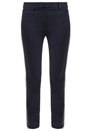 Musta takki mustan topin päällä, yhdistettynä tummansinisiin slim-fit-housuihin ja kuvioituihin mustiin tennareihin. Suora muotoilu ja istuva siluetti.
