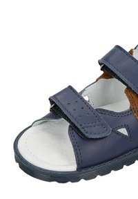 Tmavě modré kožené sandály s dvěma suchými zipy, otevřenou špičkou, bílou polstrovanou stélkou a texturovanou gumovou podrážkou. Hnědé akcenty.