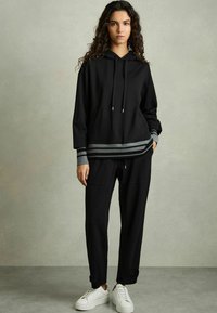 Czarna bluza z kapturem z szarym paskiem na dole, w połączeniu z czarnymi joggerami. Outfit charakteryzuje się luźnym krojem i wygodnym materiałem, z białymi sneakersami.