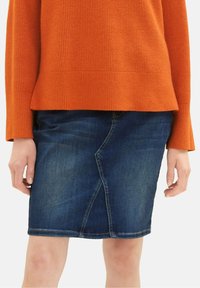 Džínová sukně v tmavě modré barvě s diagonálním švem, s obšitým lemem a přiléhavým střihem. V kombinaci s texturovaným oranžovým svetrem.