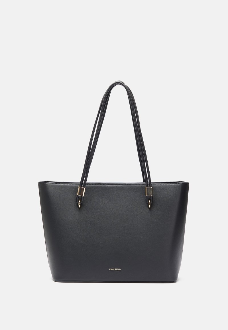 Sac cabas rectangulaire en cuir noir avec doubles poignées et petit logo doré "ANNA FIELD" en bas au centre.