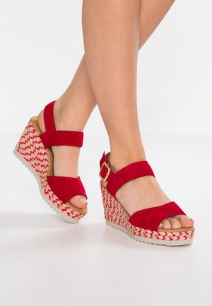 Czerwone zamszowe sandały na koturnie z otwartym palcem, z plecionym wzorem wykładanym juty na koturnie i pasek z klamrą na kostce.
