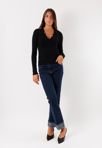 Top nero a coste con maniche lunghe e scollatura a V, abbinato a jeans in denim scuro con risvolto e décolleté nere a punta.