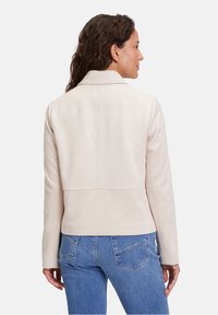 Ljusbeige mockajacka med slim fit, med krage och bakre sömmar. Matchas med blå denimjeans.