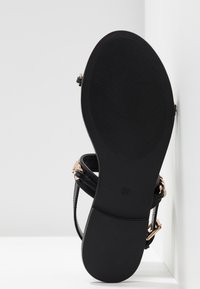 Sandale noire avec une tige en cuir lisse, fines lanières et quincaillerie en or rose. Dotée d'une semelle extérieure en caoutchouc noir texturée. Taille indiquée 37.