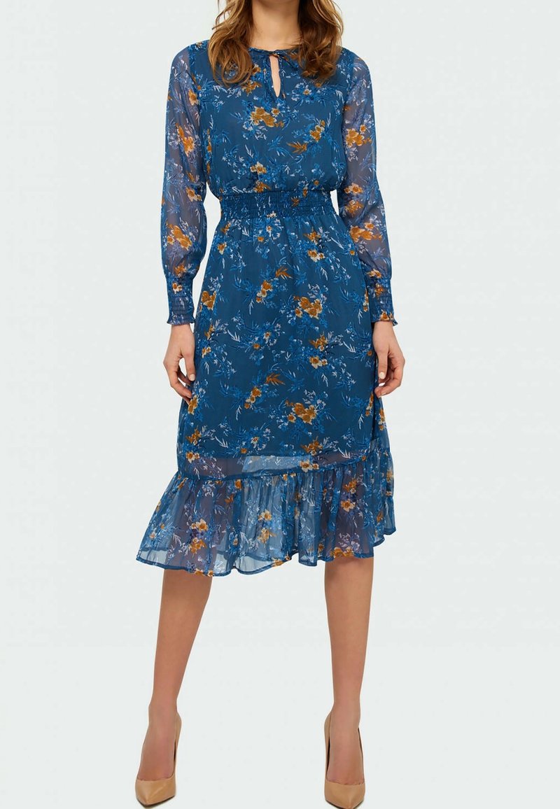 Robe bleue à motifs floraux avec de longues manches transparentes, taille smockée et ourlet à volants, présentant des motifs de fleurs orange et blanches.