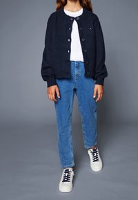 Cárdigan de punto azul marino con cierre de botones, camiseta blanca, jeans de mezclilla azul y zapatillas blancas con cordones azul marino, mostrando un ajuste relajado y textura.