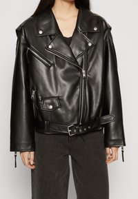 Black leather biker jacket with a cropped design, asymmetrical zippers, snap buttons, and a belted waist. Features textured finish and wide lapels.