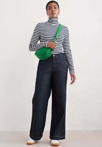 Svītrainā, pieguļošā turtleneck jakā jūras zilā un baltajā krāsā; tumšas, platas bikses; zaļa plecu soma; baltas kurpes ar gumijas zoli. Vienkārša fona.