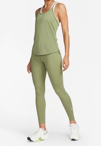 Olivově zelený tílko s bílým lemem, v kombinaci s ladícími legínami. Vyznačuje se lehkým, pružným materiálem a obepnut�ým střihem.