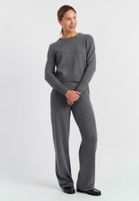 Maglione grigio lavorato a maglia con collo rotondo e orlo a costine, abbinato a pantaloni larghi coordinati. Texture morbida e vestibilità rilassata in tutto.