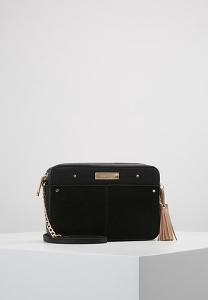 Zwarte rechthoekige crossbodytas met gouden kettingriem en roze tassel, tentoongesteld op een wit voetstuk tegen een effen achtergrond.